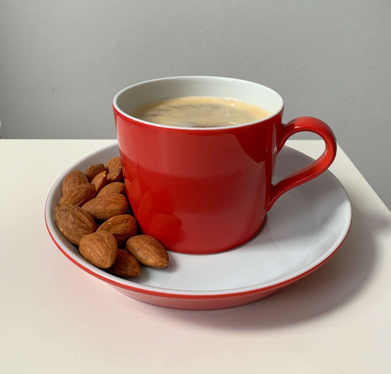rote Prognos-Tasse gefüllt mit Kaffee, daneben Mandeln
