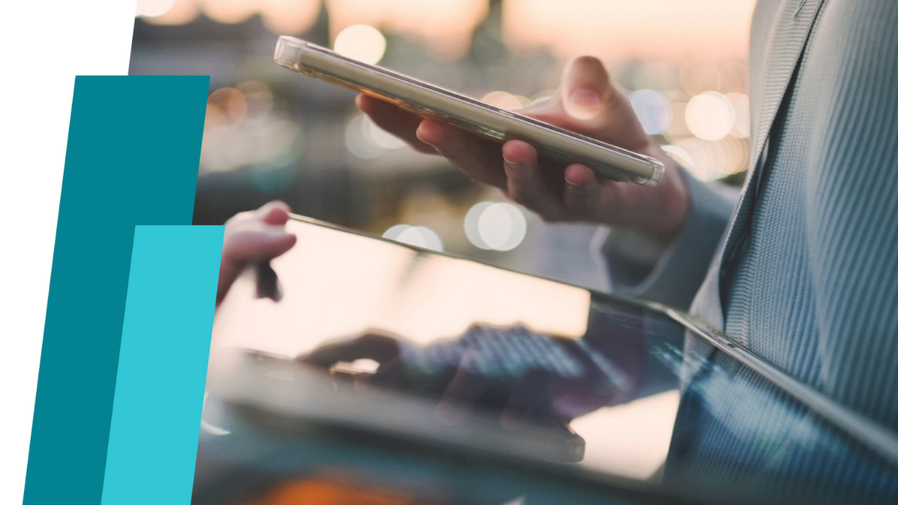 Nahaufnahme von einem Tablet und Handy in der Hand einer Person. Im Hintergrund sieht man eine Stadt.