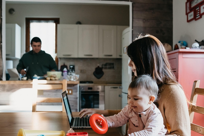 Fotos      Bilder      Fotos     Grafiken     Vektoren     Videos  Ein kleines Mädchen mit einem Laptop mit ihrer Mutter, während der Vater in der Küche kocht