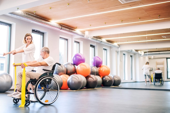 unge Frau Physiotherapeut arbeitet mit einem älteren Mann im Rollstuhl