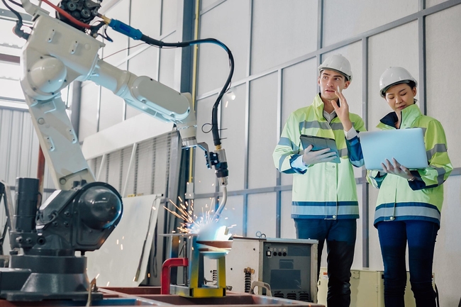 Zwei Personen stehen in der Produktion vor einem Roboter