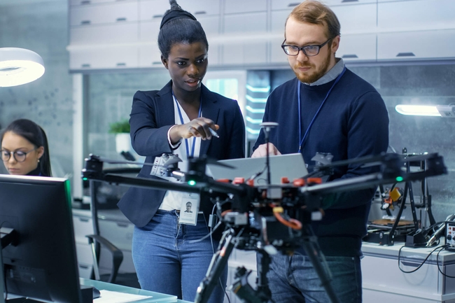 Ingenieurin und Ingenieu arbeiten an einem Drohnenprojekt mit Hilfe von Laptop und Notizen. 