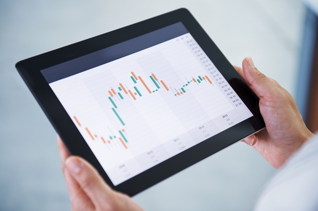 Zwei Hände halten ein Tablet, auf dessen Display ein Graph abgebildet ist. 