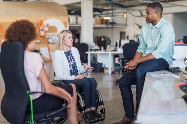 Junge Menschen in einem Business Meeting, eine Person sitzt in einem Rollstuhl.
