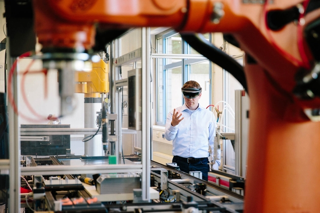 Ein Mann steht mit einer Virtual Reality Brille in einer Produktionshalle 