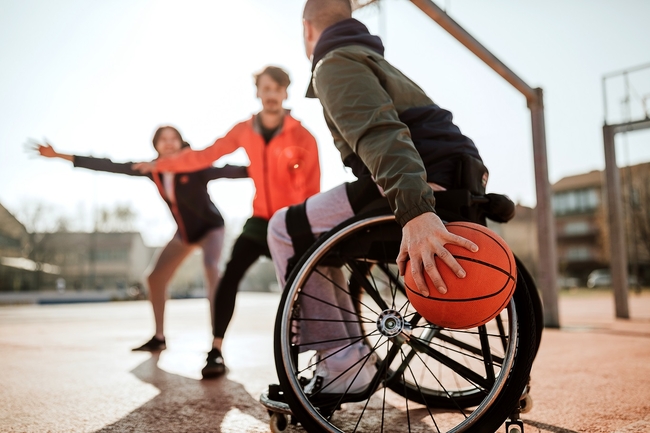 Mann im Rollstuhl, der mit Freunden auf dem Sportplatz Basketball spielt