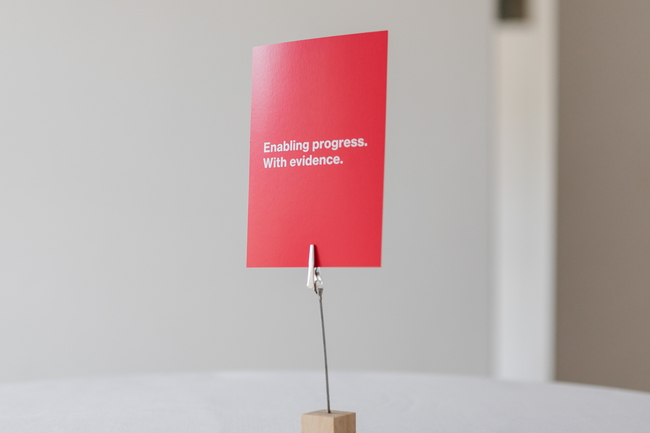 Auf einem Tisch steht eine rote Karte mit dem Prognos-Claim: Enabling progress. With evidence. 
