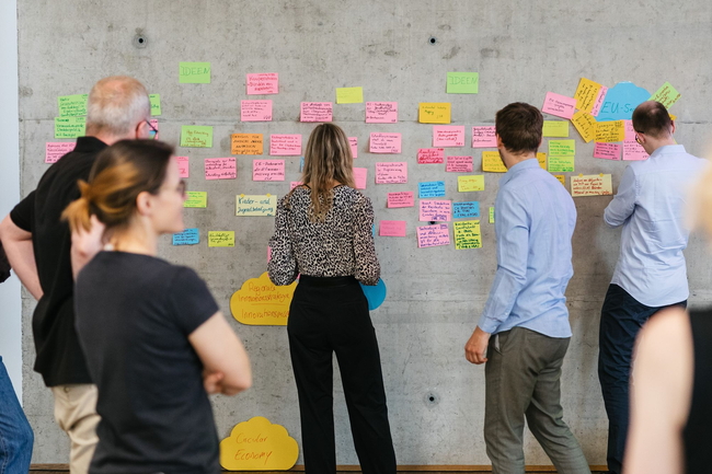 Eine Gruppe von Personen stehen an einer Wand und lesen PostIts 