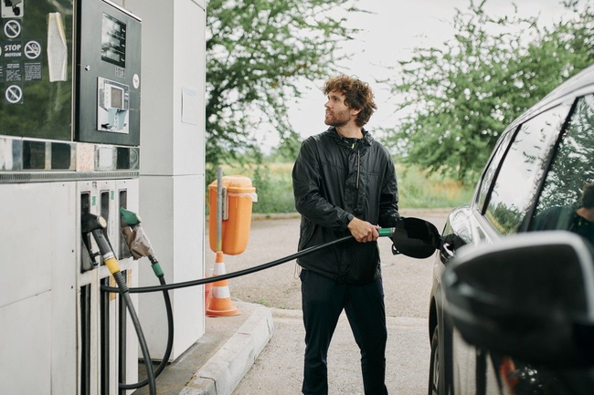 Mann steht an Zapfsäule und tankt sein Auto