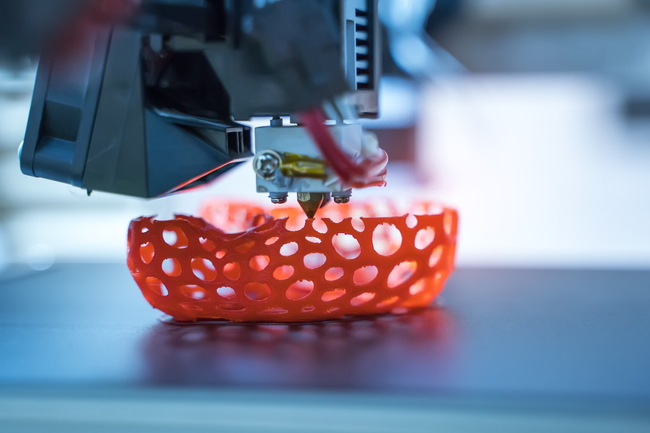 Ein 3D-Drucker druckt ein rotes Gefäß mit Löchern. 