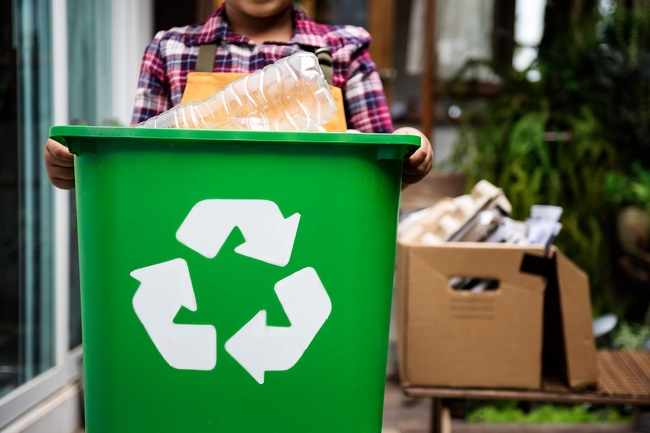 Mädchen trägt eine Tonne mit Recyclingsymbol 