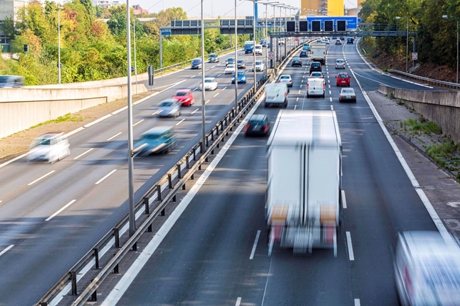 Eine Autobahn mit PKW und LKW im Sonnenschein.