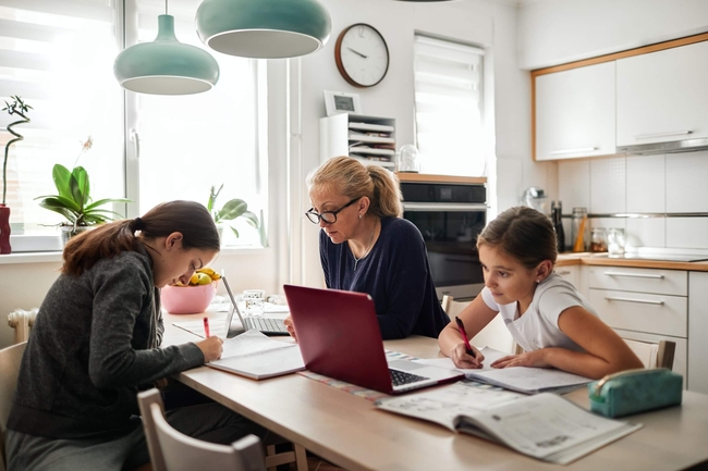 Eine Mutter und ihre zwei Töchter arbeiten mit Laptops an einem Küchentisch