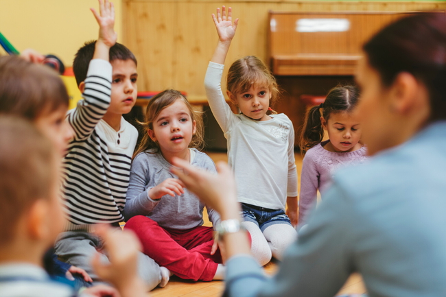 Kinder sitzen in einem Kreis im Kindergarten und melden sich.