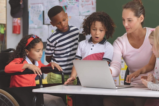 Schülerinnen, Schüler und Lehrerin am Laptop