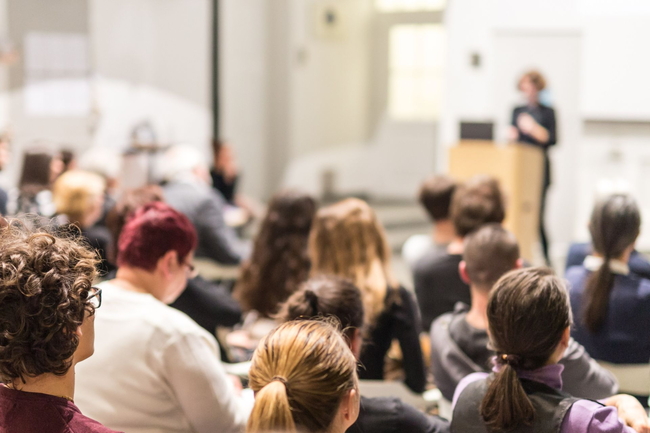 Hörsaal, in dem Menschen einem Vortrag einer Frau zuhören