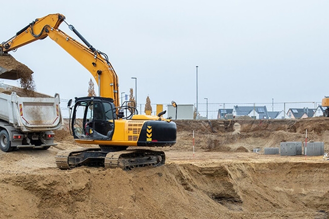 Ein Bagger hebt Sand aus einer Grube in einen LKW