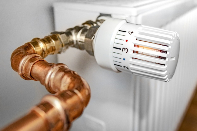 Nahaufnahme eines weißen Heizkörperthermostats mit Kupferrohr