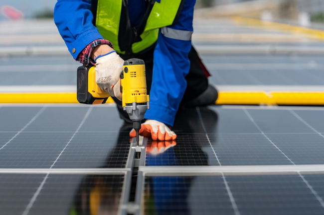 Eine Person befestigt Solarpanel auf einem Dach. In Nahaufnahme