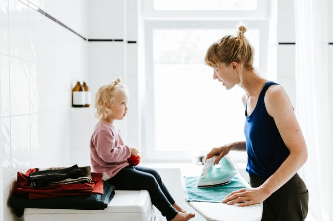 Mutter betreut Kind und bügelt ein Handtuch