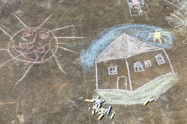 Kreidezeichnung von einem Kind, zu sehen sind ein Haus und die Sonne