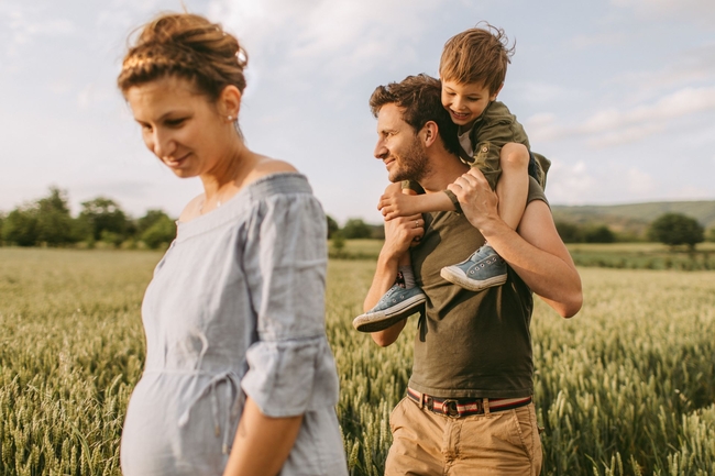 Familie spaziert über ein Feld, Mutter ist schwanger, Vater hat Kind auf den Schultern