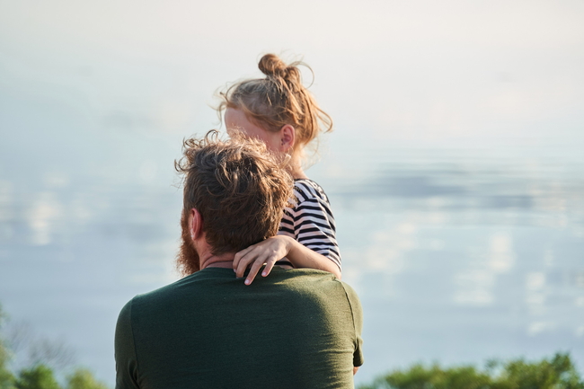 Ein Vater blickt mit seinem Kind im Arm auf das Meer.