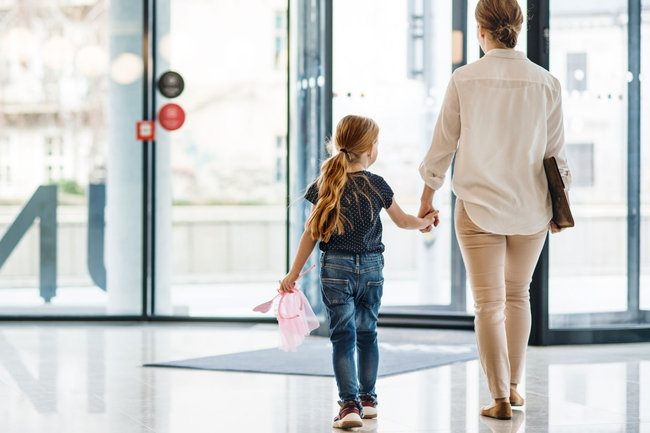Mutter und Tochter, die Hand und Hand aus einem Büro hinausgehen