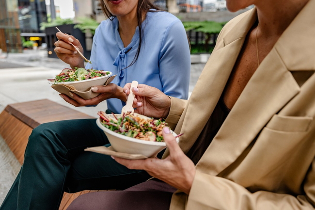 Zwei Personen sitzen draußen und essen ihr Mittagessen aus Schüsseln.