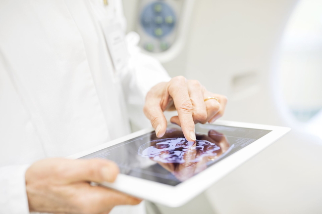 Tablet mit Röntgenbild, das von einer Person in einem weißen Kittel in den Händen gehalten wird