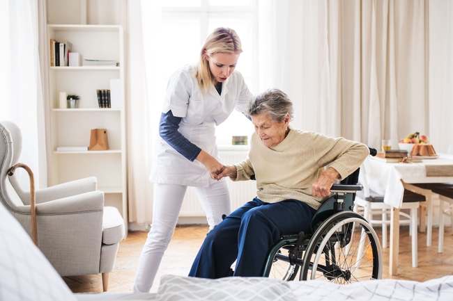 Pflegefachkraft, die einer Seniorin aus dem Rollstuhl hilft