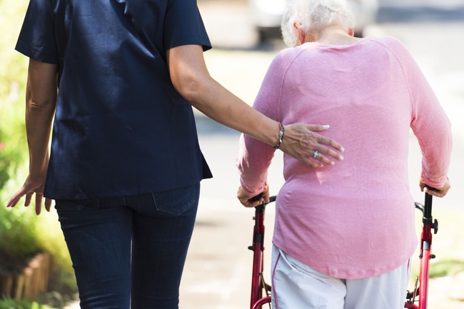 Seniorin geht an einem Rollator, Pflegefachkraft stützt sie 