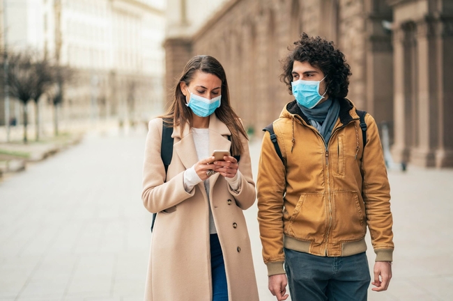 zwei junge Menschen mit Mund-Nasen-Schutz laufen nebeneinander auf einer leeren Straße