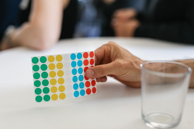 Eine Hand hält einen Zettel mit Klebepunkten für ein Meeting.