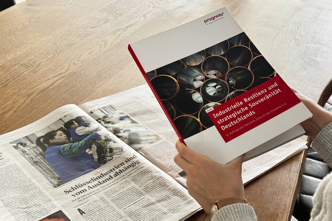 Person hält Studie in der Hand, Zeitungsartikel liegt auf dem Tisch