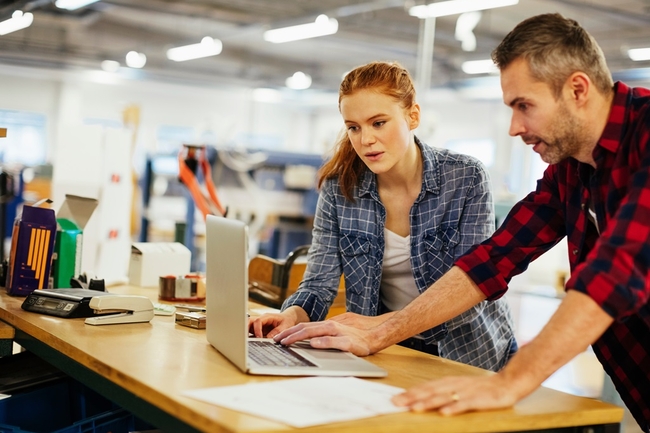Zwei Personen stehen in einer Arbeitssituation am Laptop
