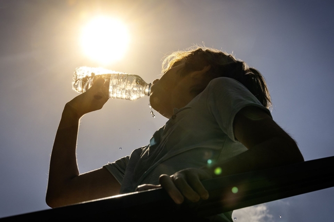 Ein Kind steht in der prallen Sonne und trinkt aus einer Wasserflasche