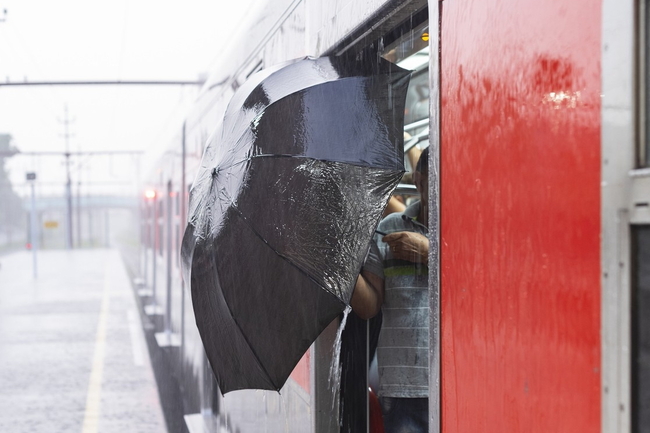Roter Zug am Bahnhof, es regnet, Person steigt mit einem Regenschirm ein