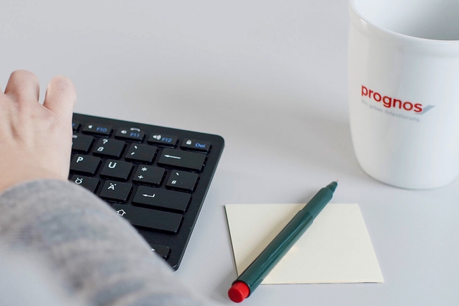 Eine Person tippt auf der Tastatur, neben ihr liegen ein Notizbuch und ein Stift