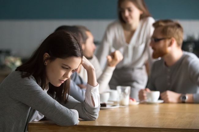 Trauriges Mädchen sitzt mit anderen Menschen an einem Tisch