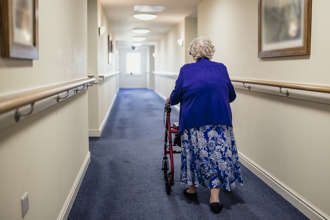 Seniorin geht an einem Rollator durch den Flur in einem Pflegeheim