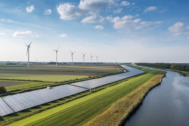 Auf der rechten Seite ein Fluss, daneben eine Solarkraftanlage, dahinter Windkraftanlagen 