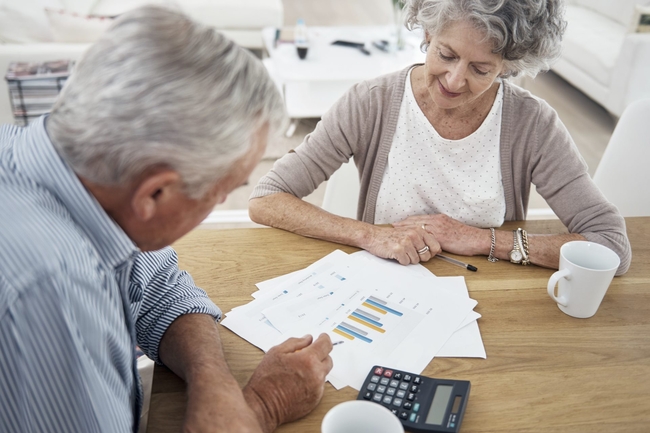 Rentnerin und Rentner am Tisch mit Taschenrechner und Statistiken