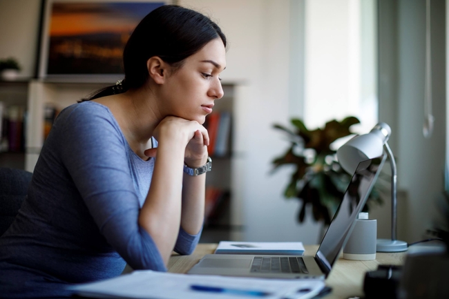 eine junge Frau sitzt vor ihrem Laptop am Schreibtisch