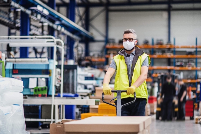 ein junger Mann in Warnweste schiebt Ware auf einem Wagenheber durch eine Produktionshalle