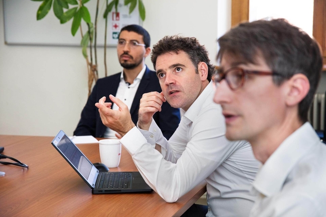 Drei Personen sitzen am Tisch mit einem Laptop und unterhalten sich.