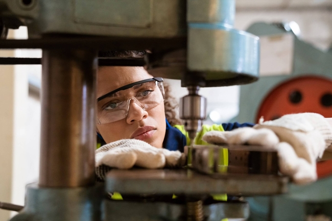 Weibliche Ingenieurin mit Schutzbrille arbeitet an einer Fertigungsanlage.