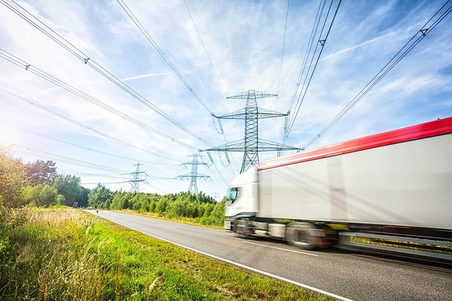 LKW fährt auf der Straße, im Hintergrund Strommaste