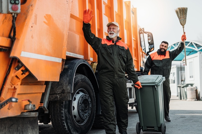 Zwei Männer, die den Müll abholen, dahinter ein Müllwagen