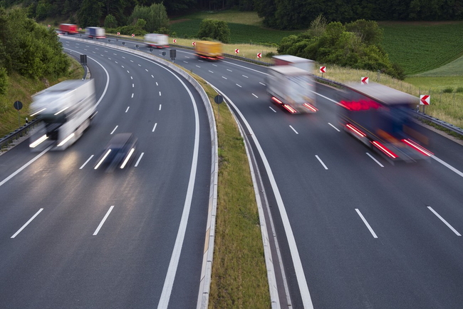 Mehrspurige Autobahn mit schneller Verkehrsspur, Fahrzeuge als Lichtspuren im Dämmerlicht.